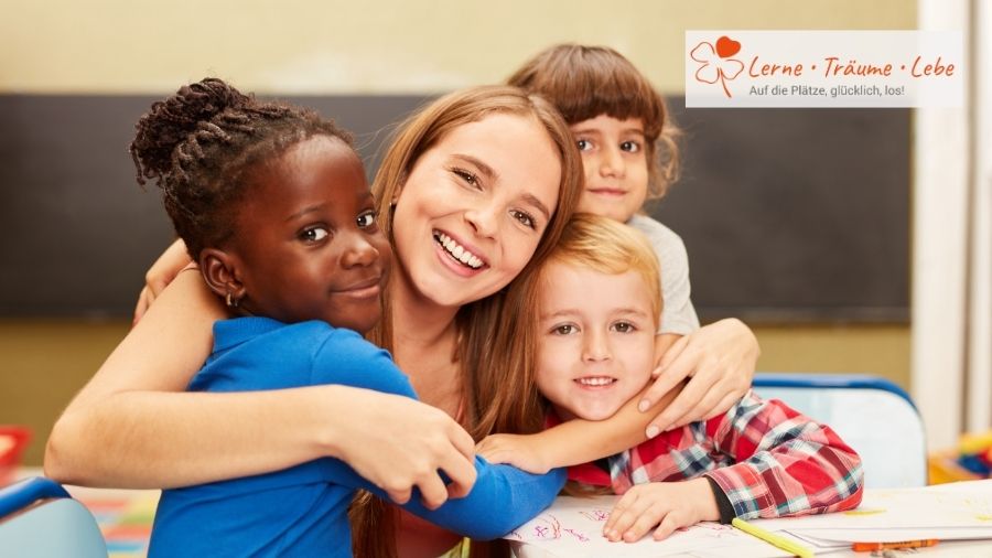 Eine Lehrerin sitzt in ihrem Klassenraum und umarmt fröhlich drei Schüler