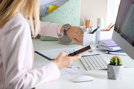 Frau arbeitet im Homeoffice am Computer und hat ein Handy in der Hand